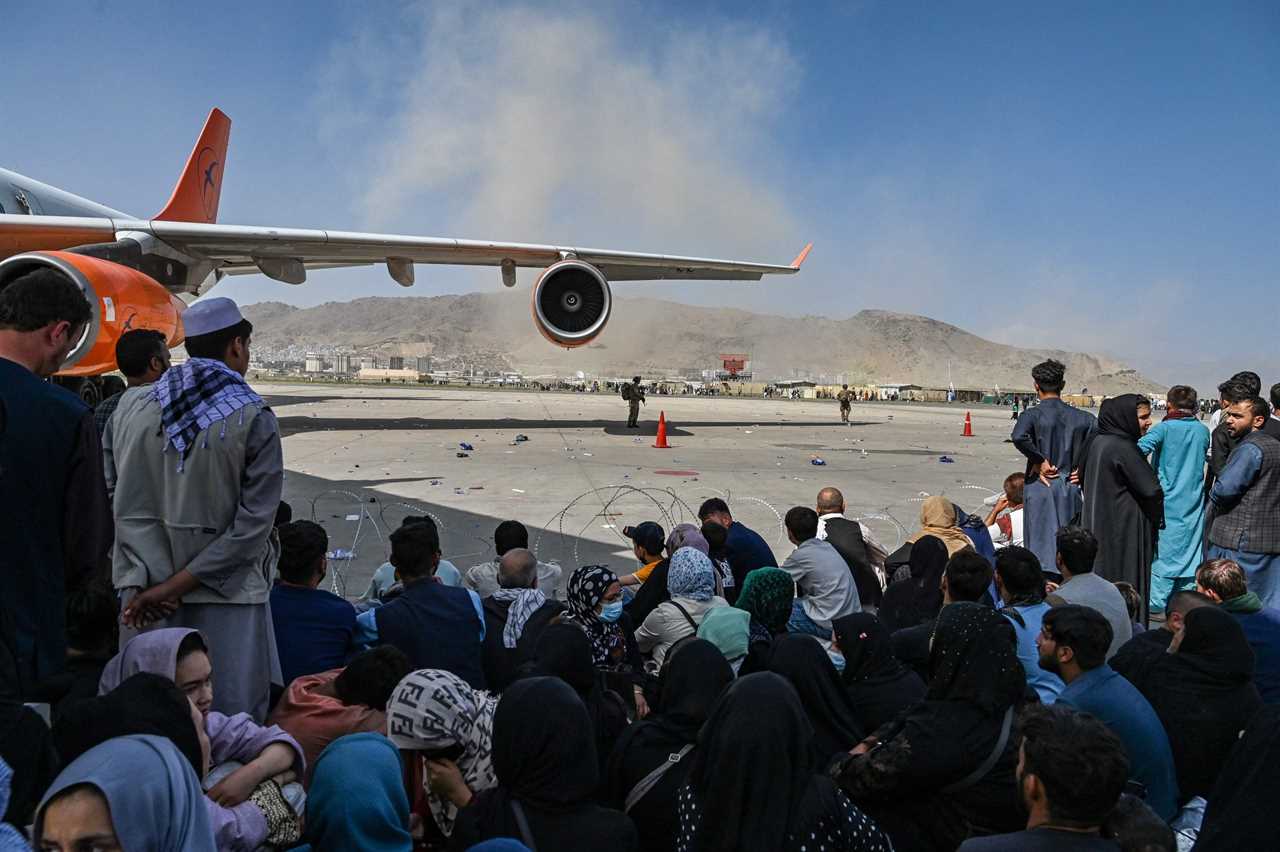 Afghan people sit as they wait to leave the Kabul airport