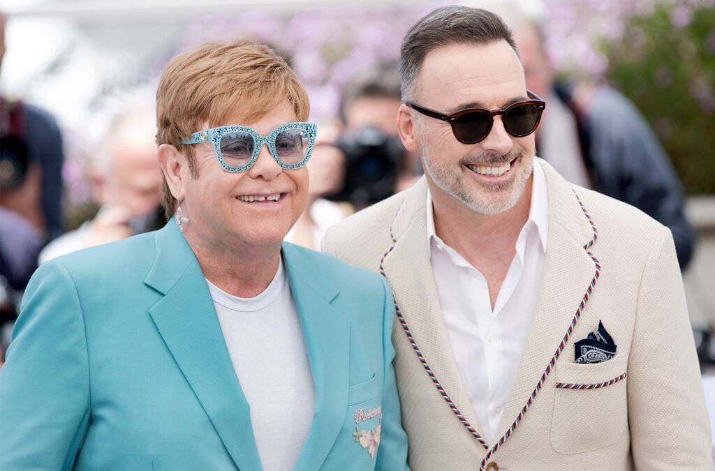 Elton John on the left in a turquoise suit and glasses, David Furnish on the right.